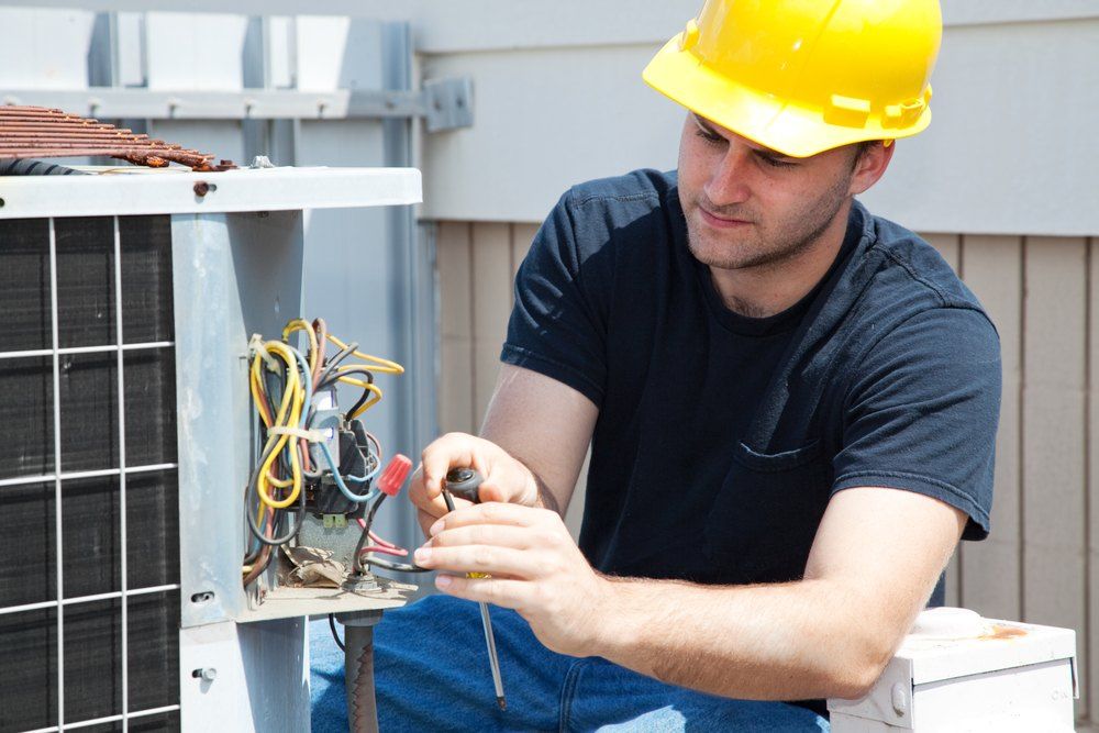 HVAC technician in hard hat repairs an air conditioning unit.