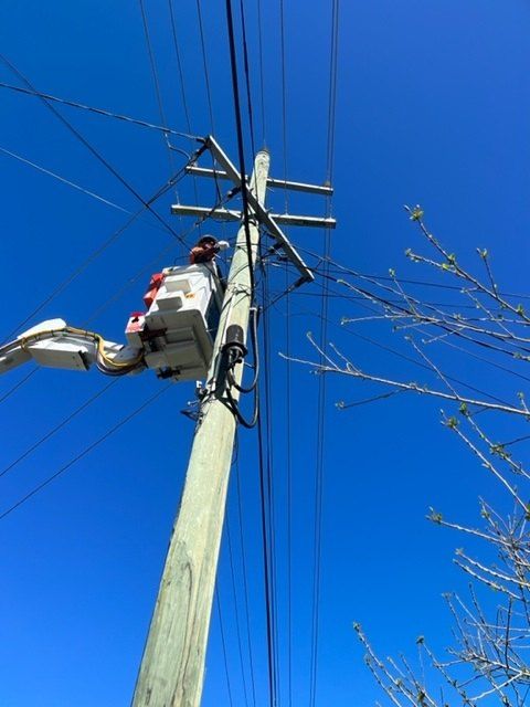 Lineman in a bucket truck working on power lines against a bright blue sky.