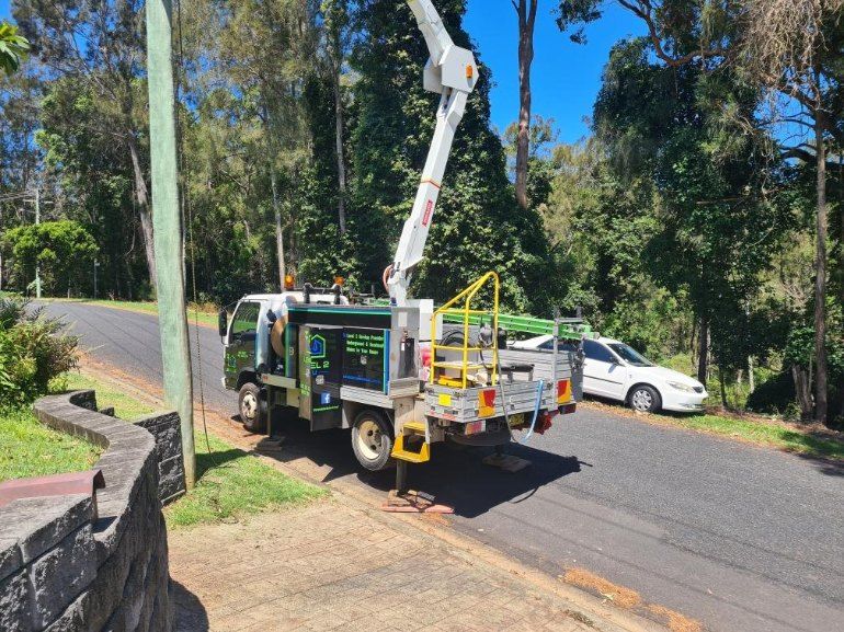 Truck with extended boom working on power lines by a road, sunny day.