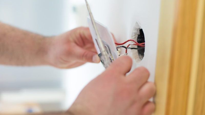 Person installing electrical wiring in a wall, holding a light switch plate.