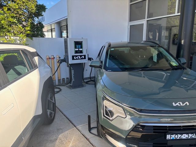 Two Kia electric vehicles charging at a charging station outside a building.
