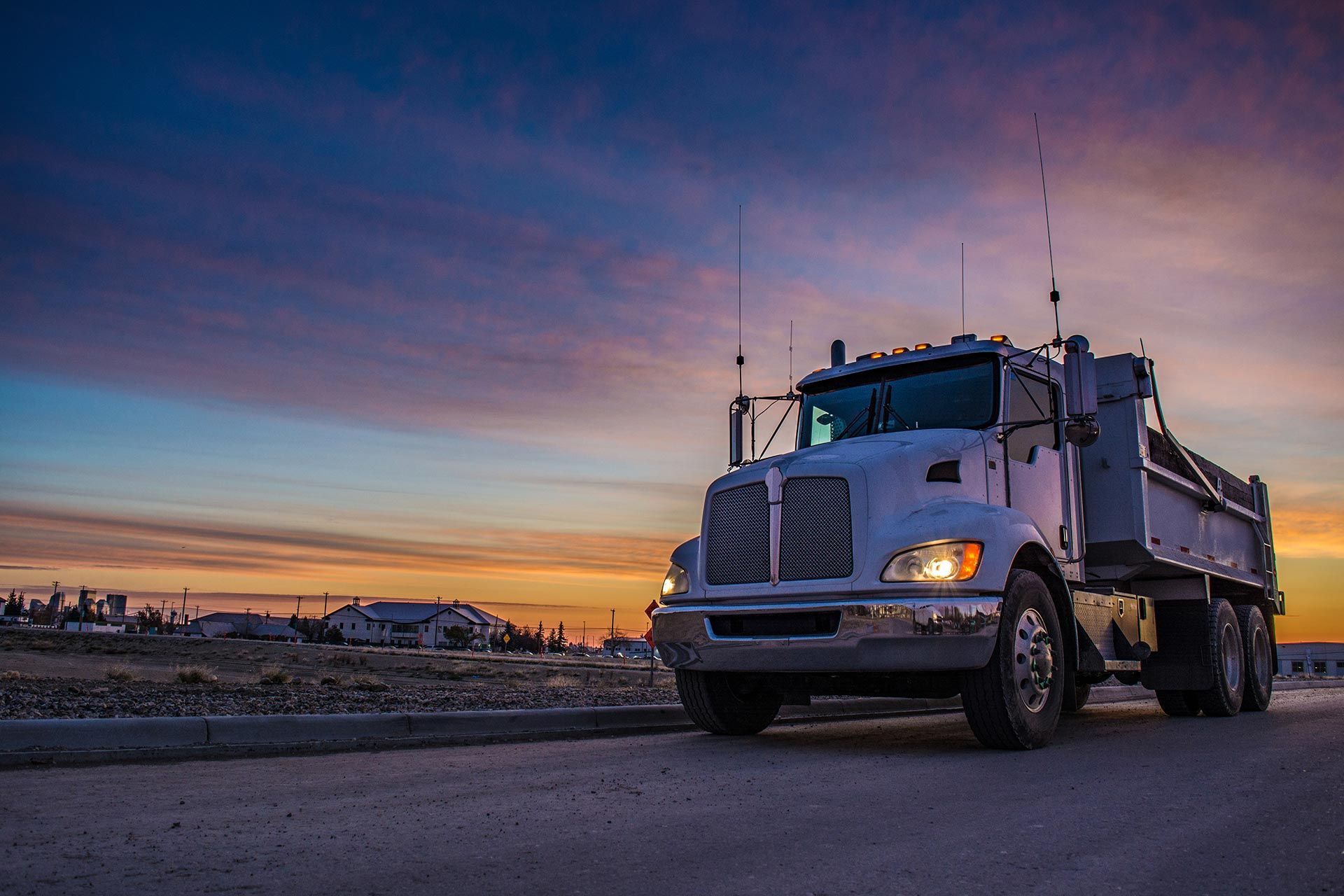 Heavy dump truck driving on a paved road at sunset with an industrial area in the distance. Heavy dump truck driving on a paved road at sunset with an industrial area in the distance.