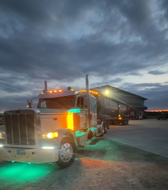 Semi-truck parked at dusk with green and orange lights illuminated.