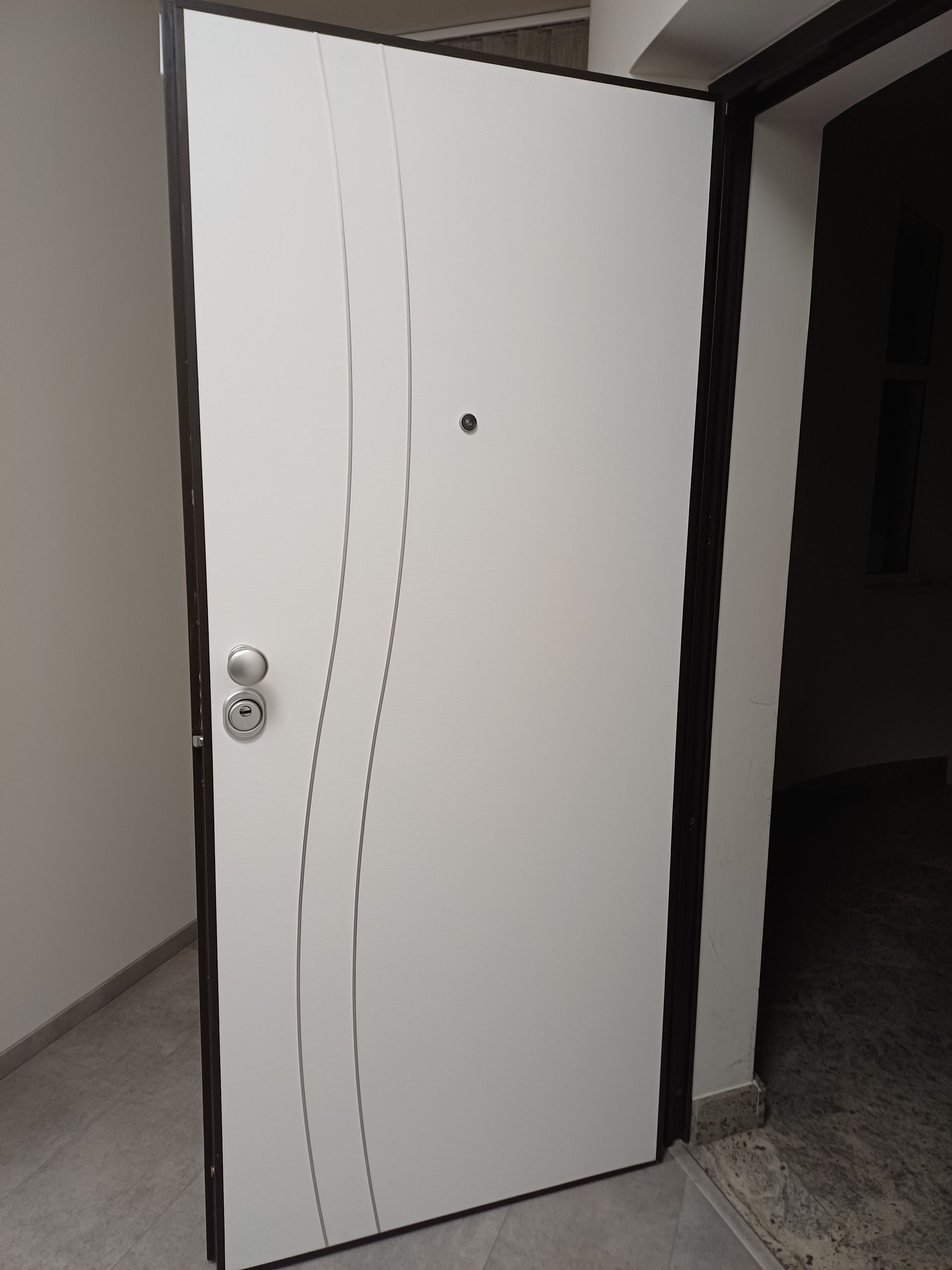 Porta d'ingresso bianca con linee verticali ondulate, leggermente aperta su un corridoio interno scuro.