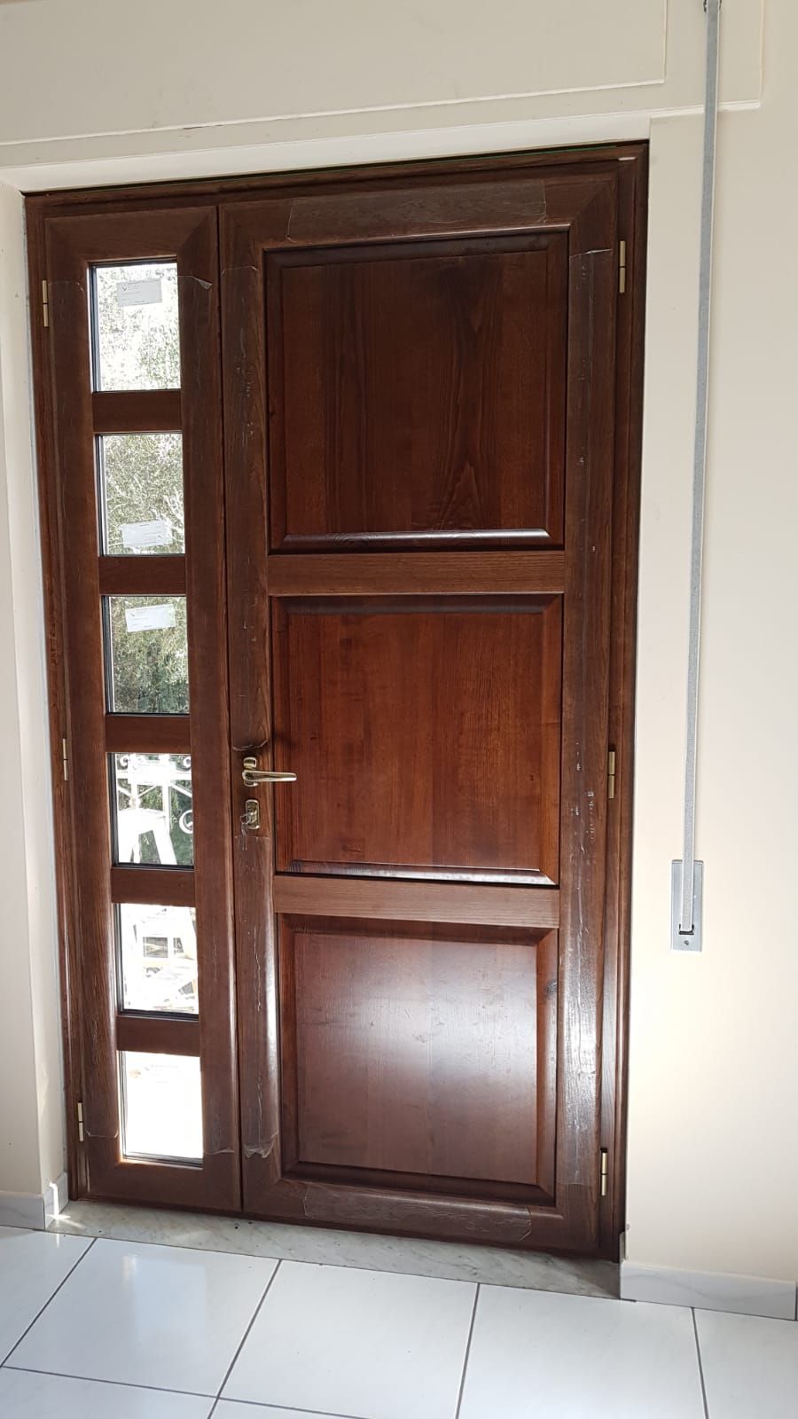 Porta d'ingresso in legno con stretti pannelli di vetro accanto a una parete beige con pavimento piastrellato