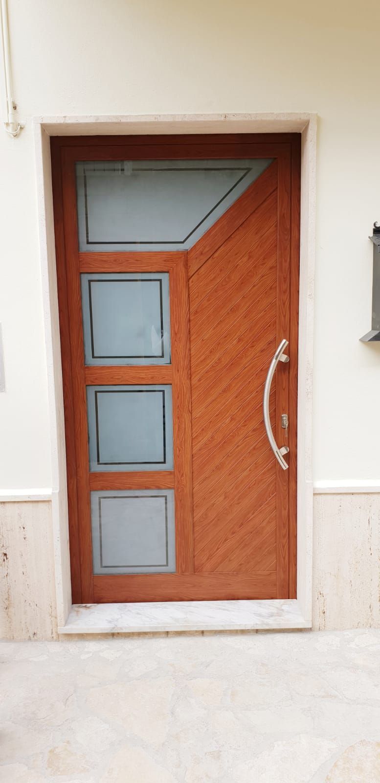 Porta d'ingresso in legno con pannelli in vetro satinato e maniglia in metallo curvato su una parete chiara