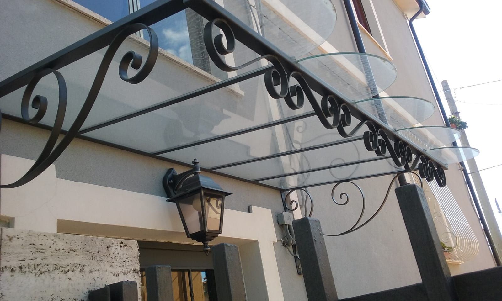 Tenda da sole in ferro battuto nero sopra l'ingresso di un edificio, con lampadario a forma di lanterna.