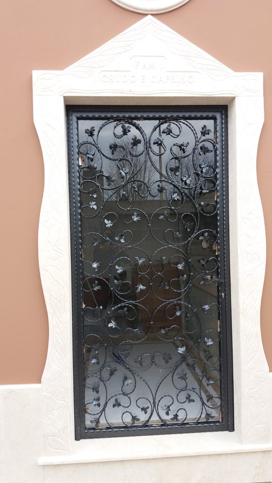 Finestra con cornice bianca e inferriata in ferro battuto nero decorata su una parete color pesca.