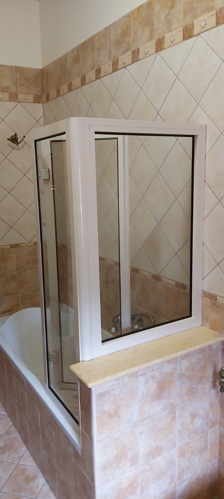 Box doccia con porta in vetro con cornice bianca e pareti rivestite con piastrelle beige.