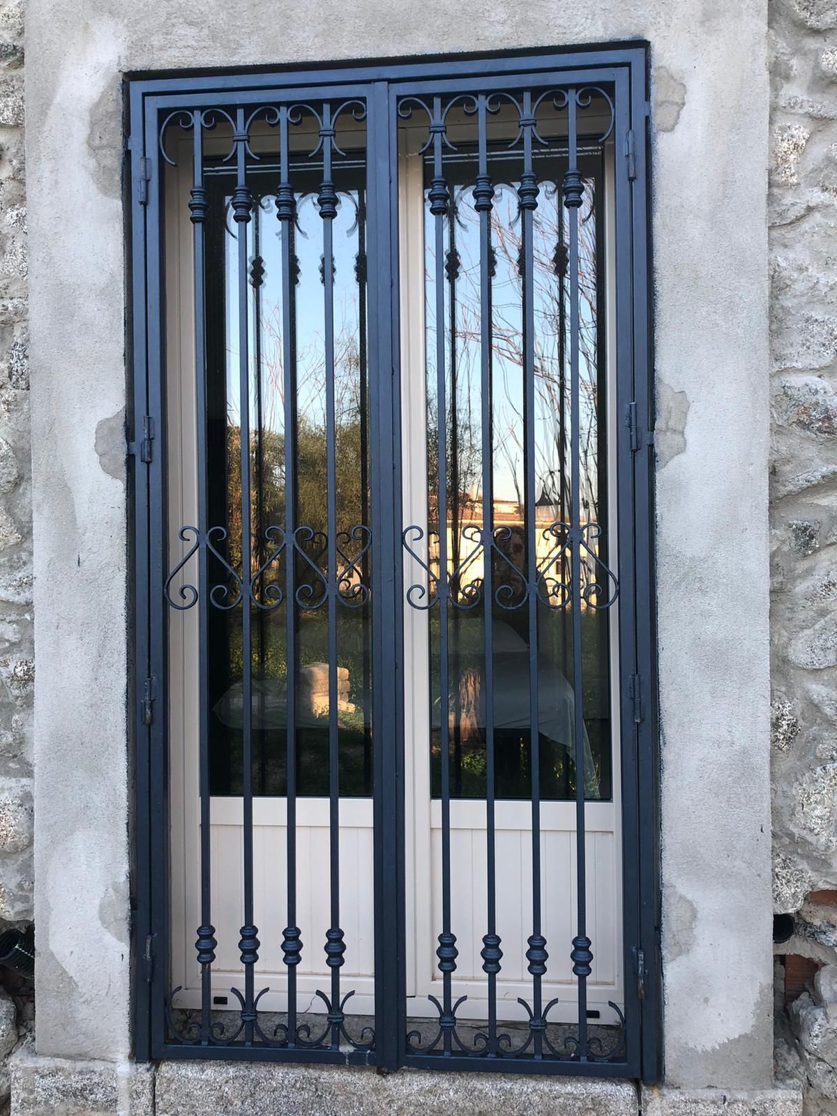 Inferriate di sicurezza in metallo blu su un muro di pietra con porta o finestra a vetri alle spalle.