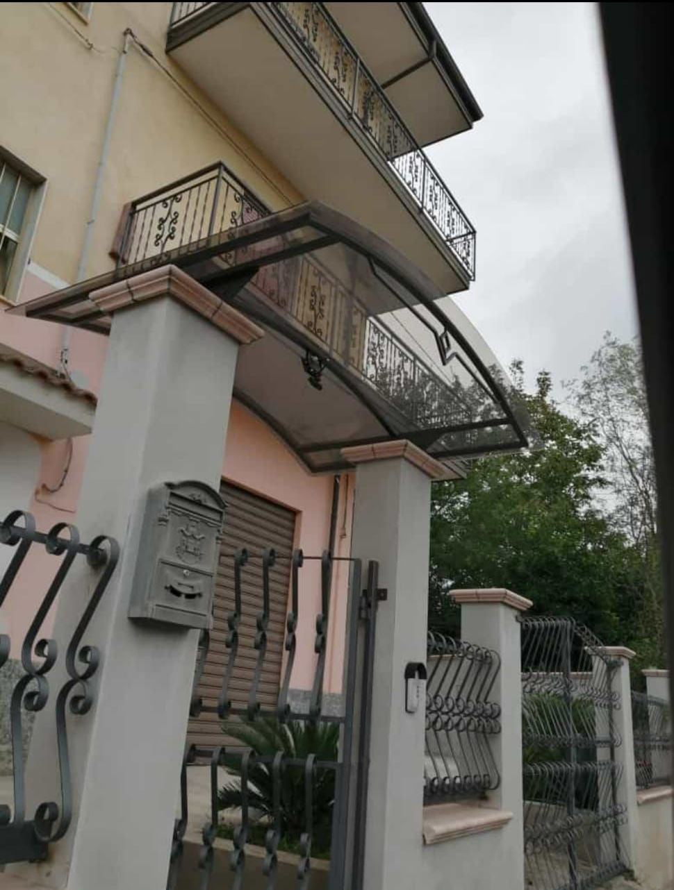 Facciata di un edificio residenziale con balconi, ringhiere metalliche e ingresso con cancello sotto un cielo nuvoloso.