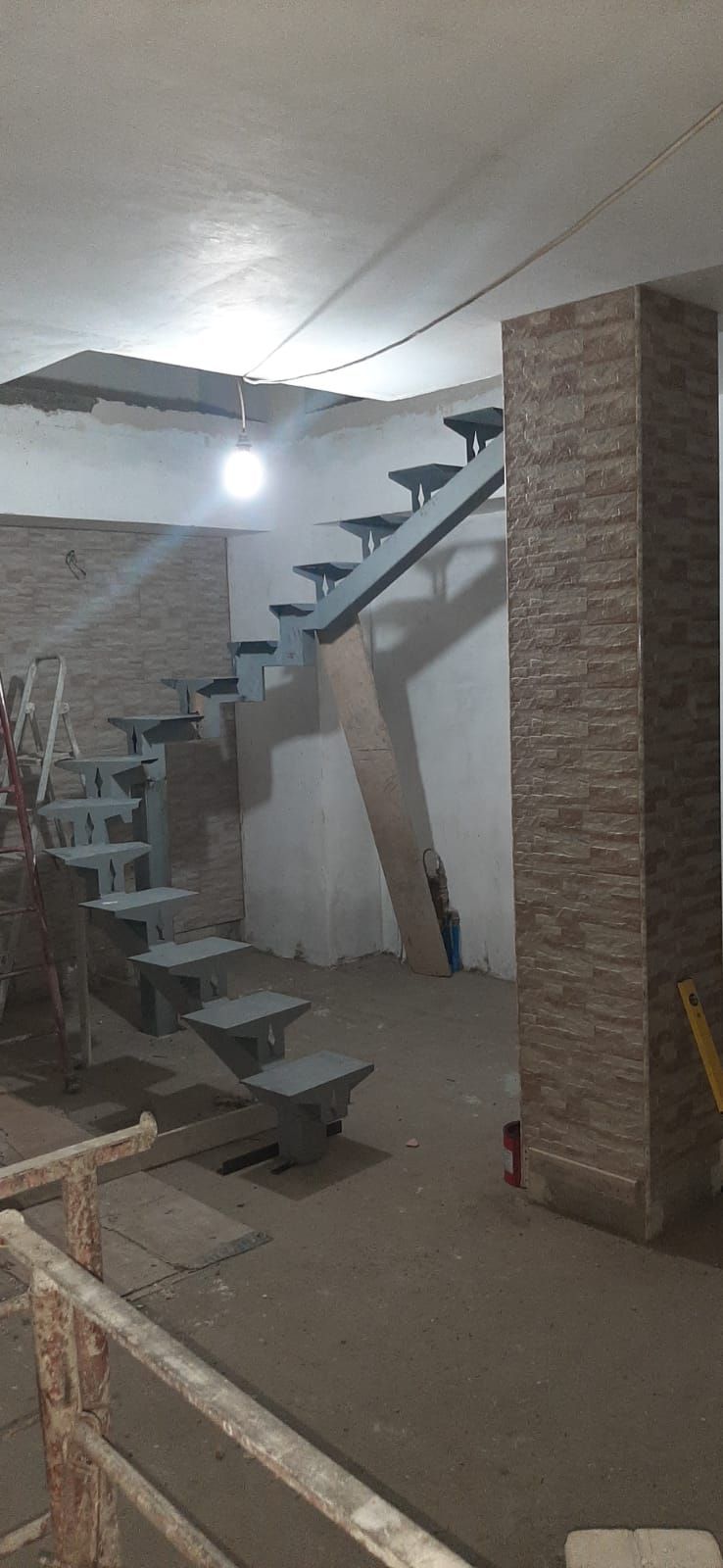 Vano scale interno non rifinito con gradini in cemento, pareti bianche e materiali da costruzione a vista.