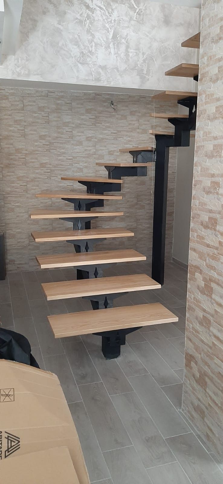 Scala in legno sospesa con gradini sfalsati addossati a una parete texturizzata in un interno moderno