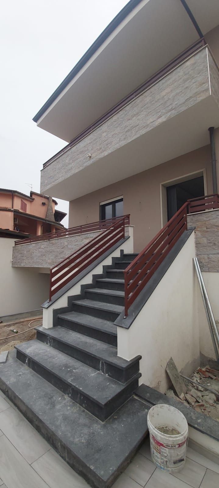 Esterno di una casa con una lunga scala in cemento e corrimano rossi che conduce all'ingresso.
