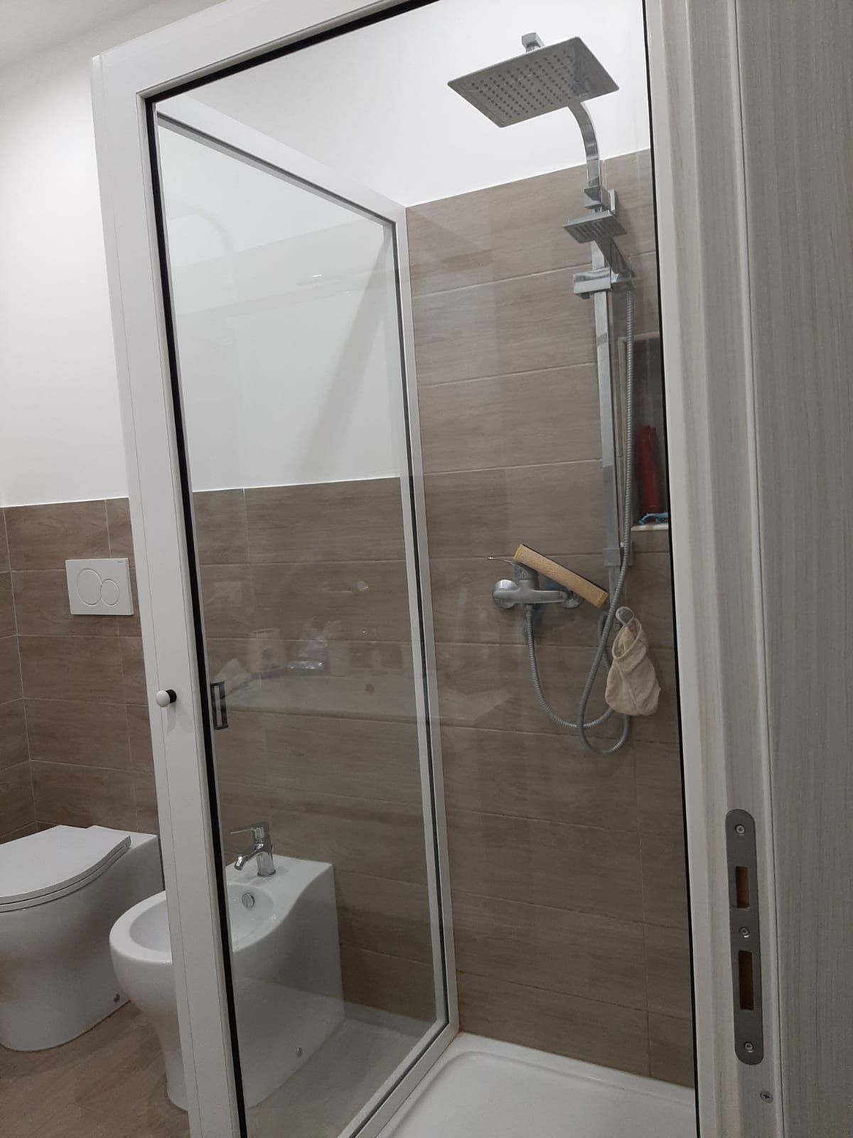Bagno con box doccia in vetro, soffione a parete e WC a vista.