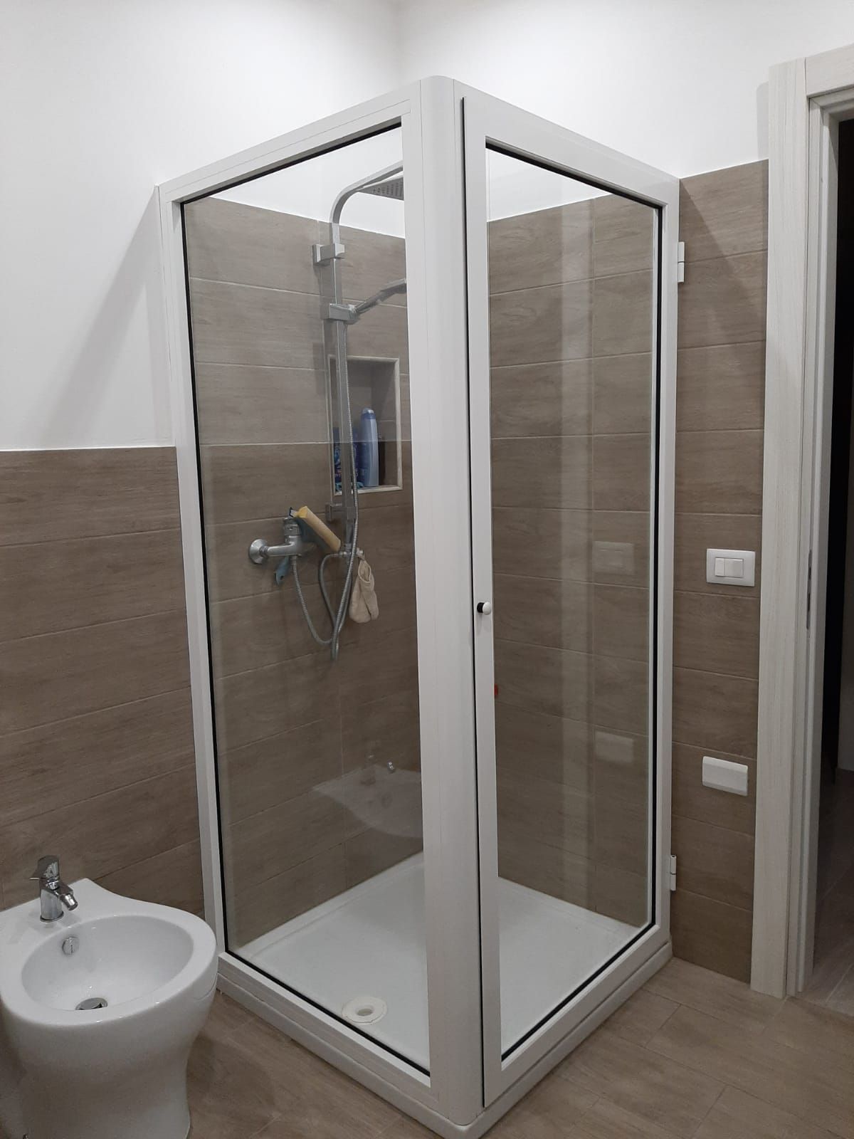 In un bagno, si trova una cabina doccia in vetro con porte bianche e pareti piastrellate beige.