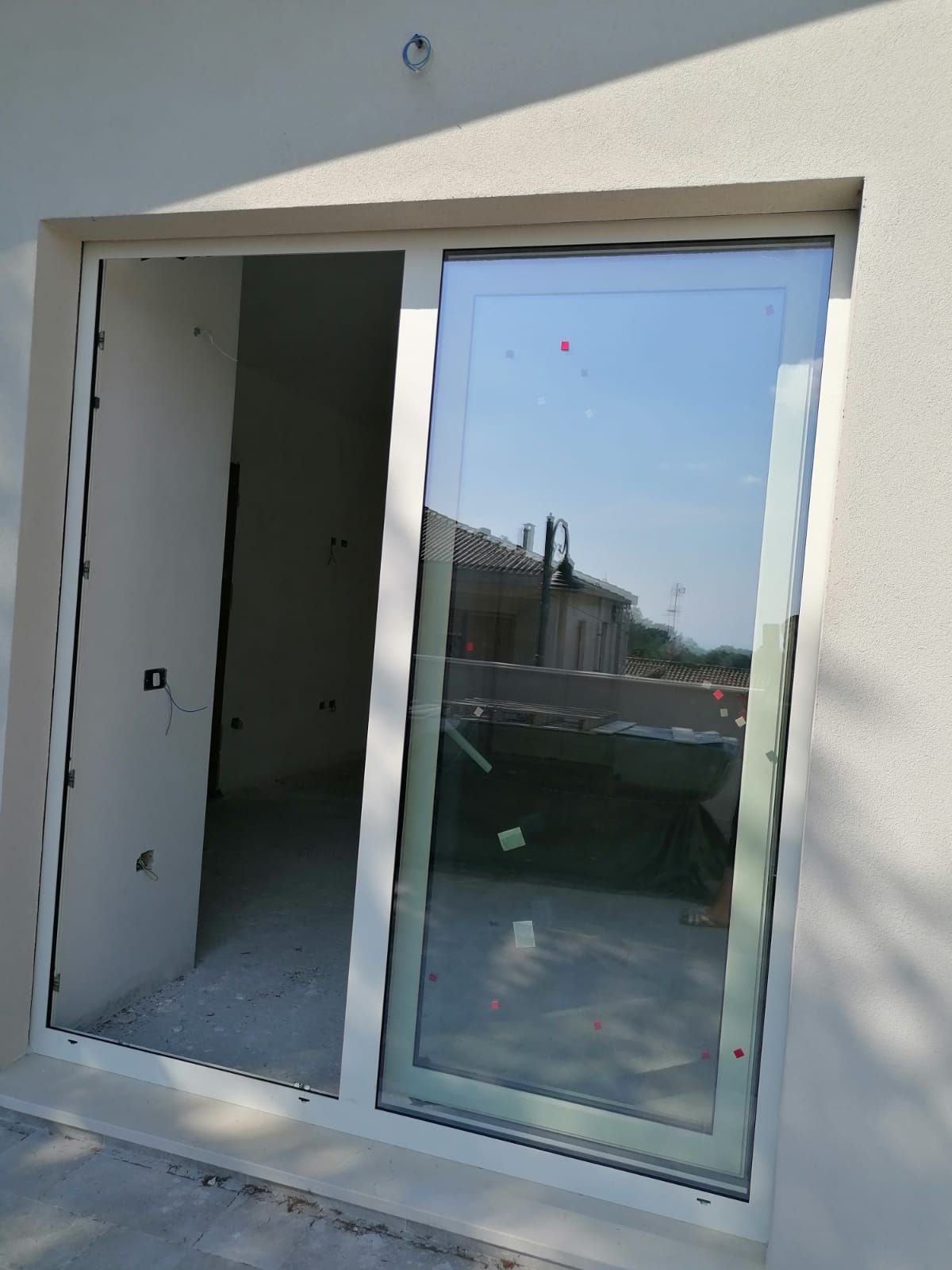 Porta scorrevole in vetro installata in una parete esterna bianca, con un pannello aperto e un pannello chiuso riflettente.
