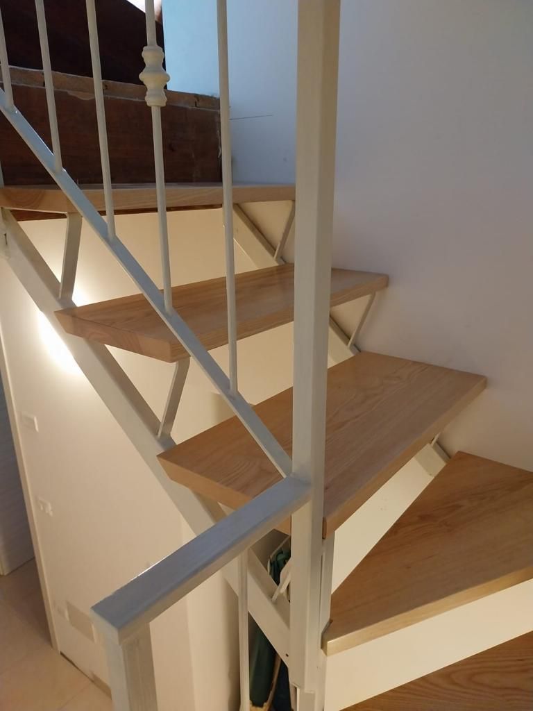 Scala interna in legno con ringhiera bianca e gradini in legno chiaro che conducono verso l'alto