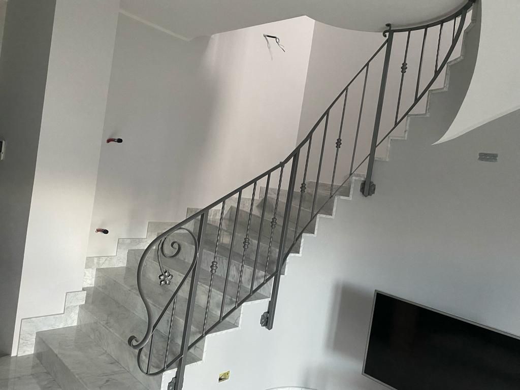 Scala bianca curva con ringhiera nera decorata in una stanza luminosa e vuota, con televisore a parete sottostante.