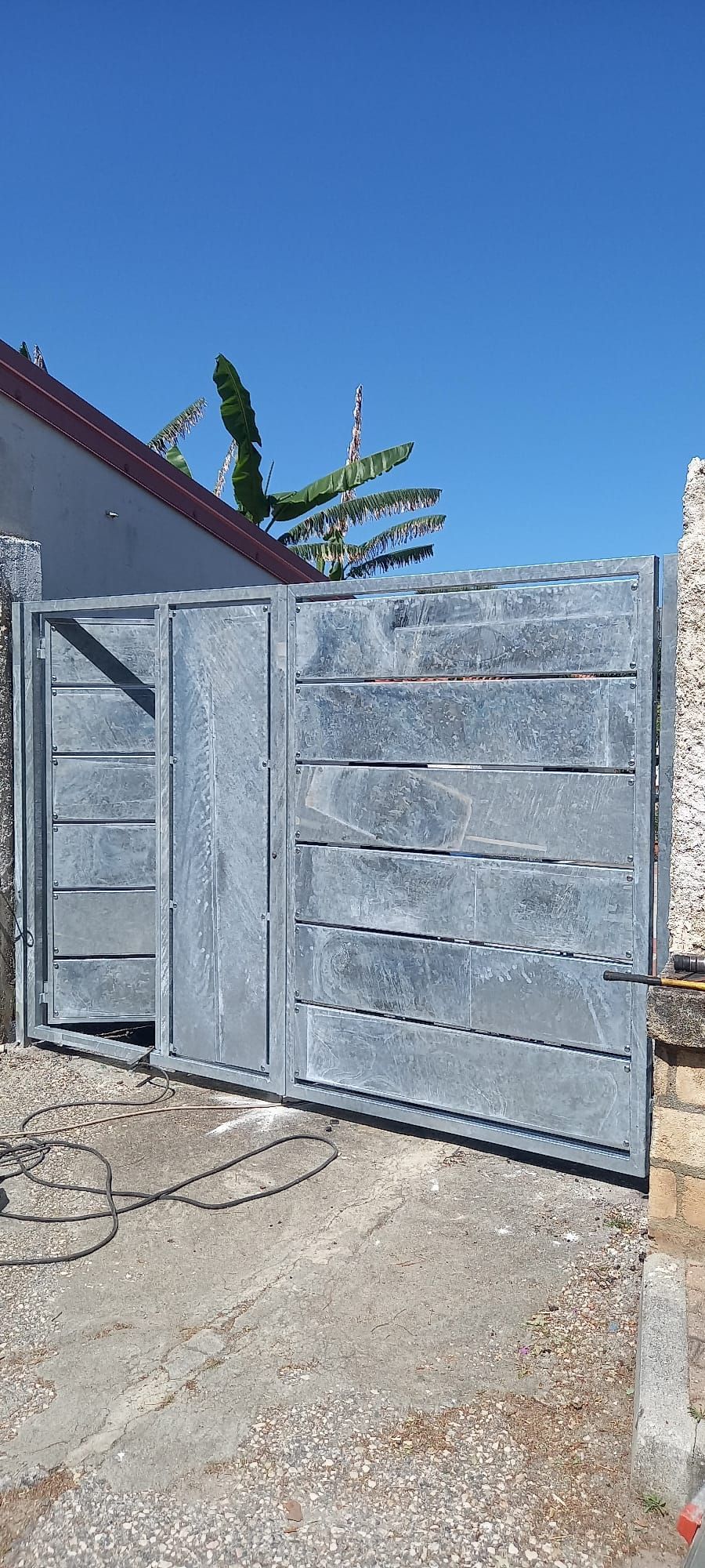 Cancello carrabile in metallo grigio accanto a un muro intonacato sotto un cielo azzurro