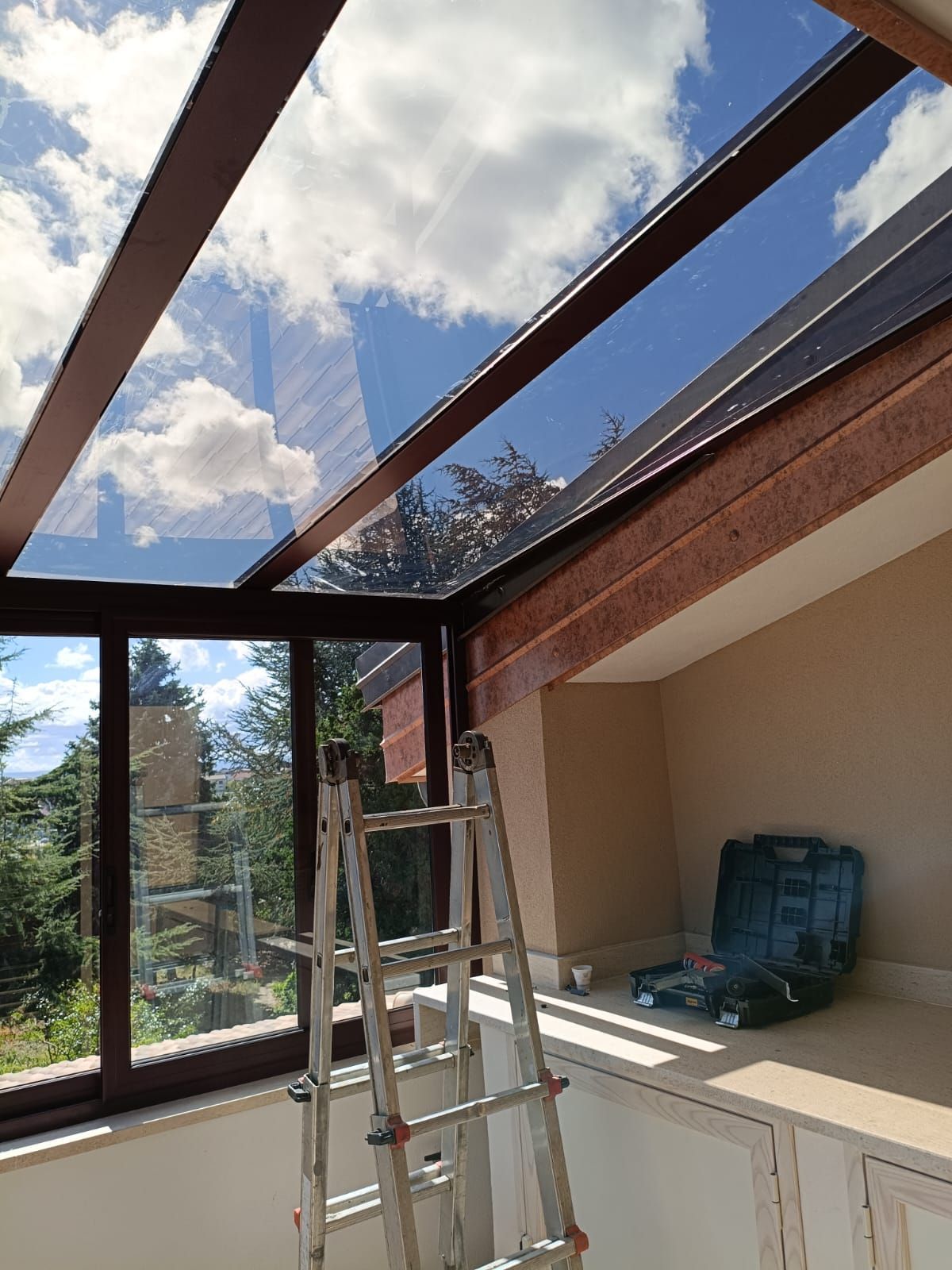 Veranda in costruzione con travi del tetto in metallo, una scala e cielo azzurro visibile attraverso la struttura aperta.