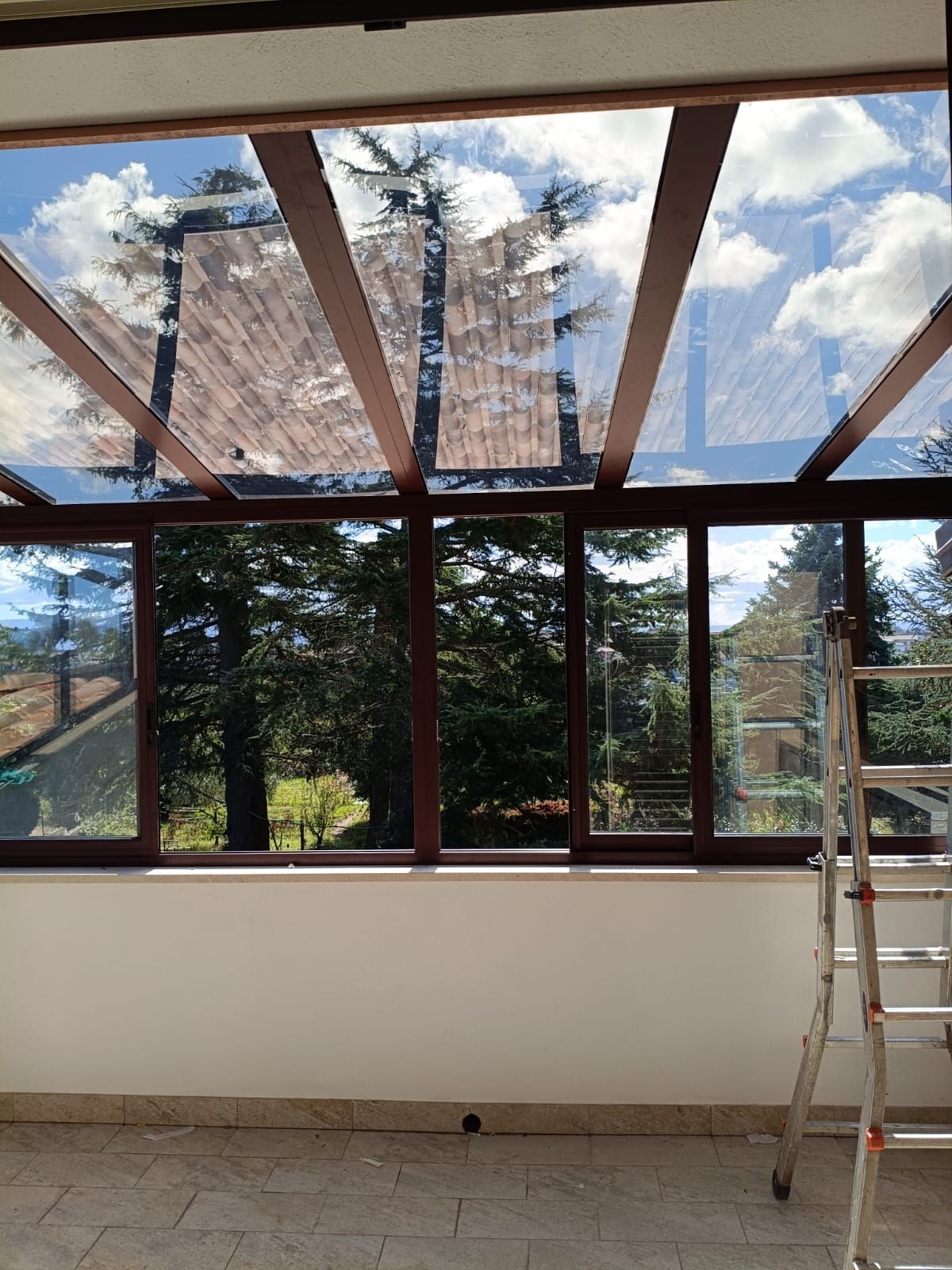 Stanza luminosa con ampie finestre, una scala e un lucernario sul soffitto non rifinito.