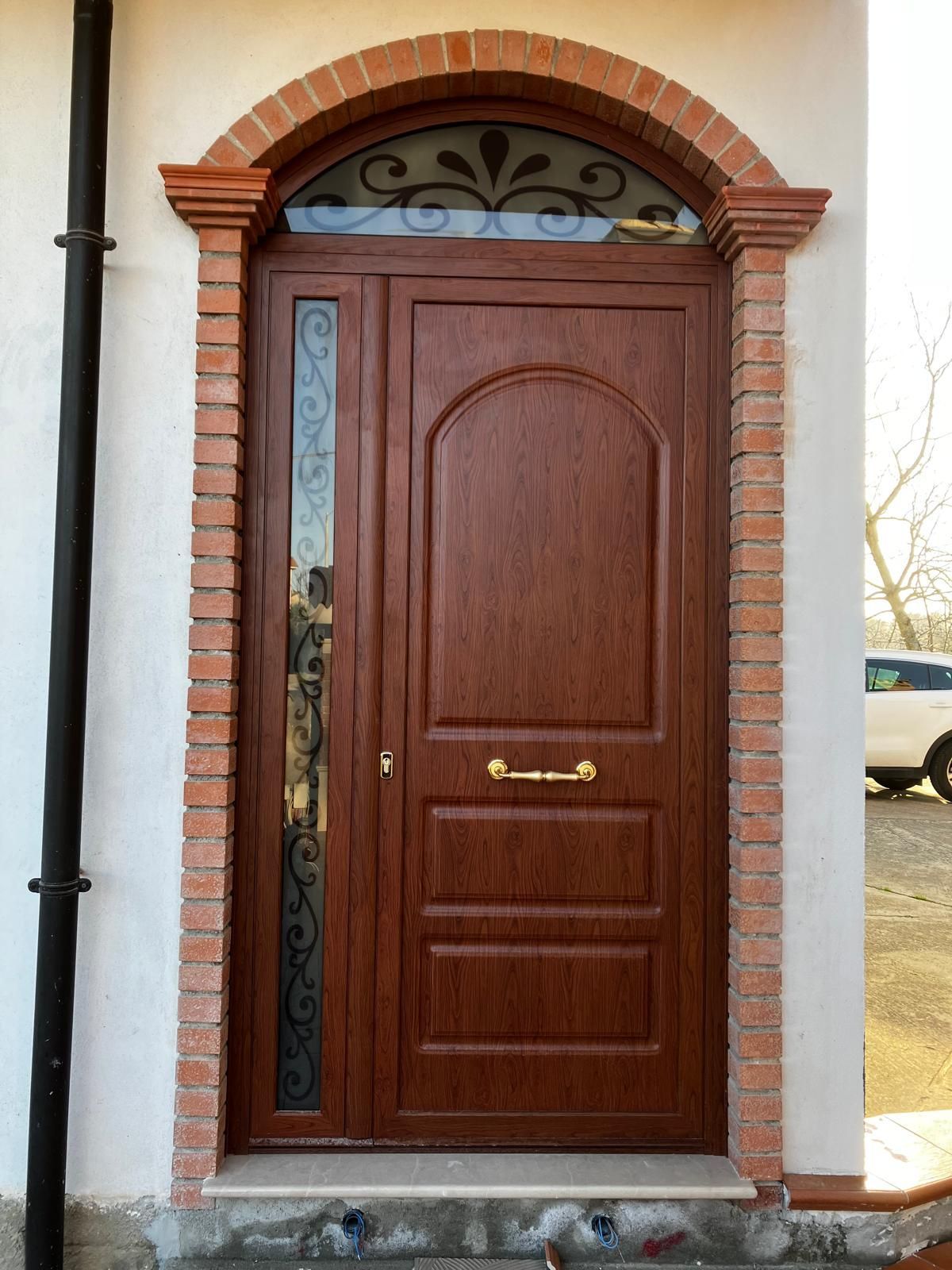 Porta d'ingresso in legno con cornice ad arco in mattoni e decorazioni in ferro battuto su una parete intonacata di bianco.