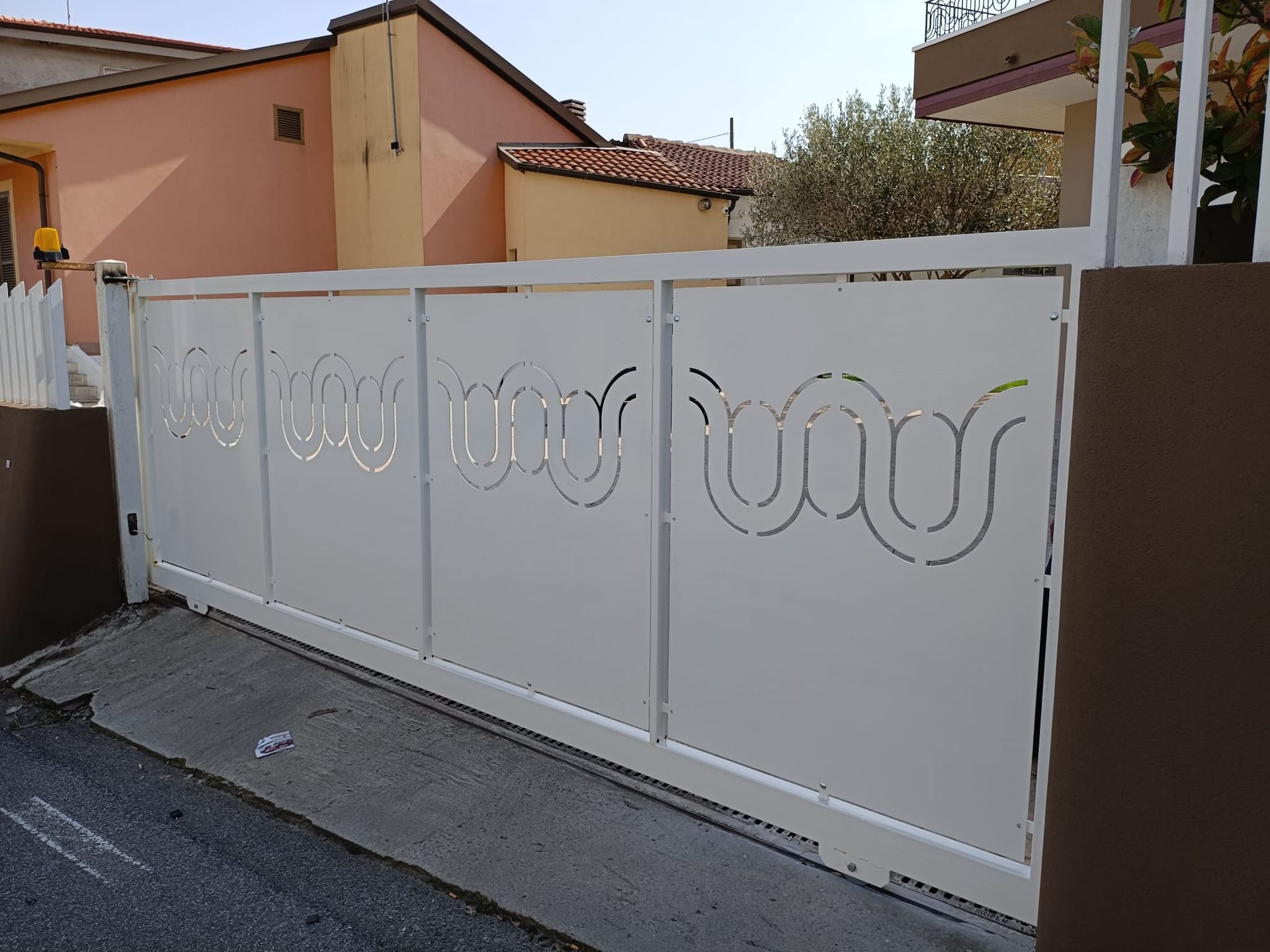 Cancello d'ingresso bianco con ritagli circolari decorativi davanti a una casa color pesca.