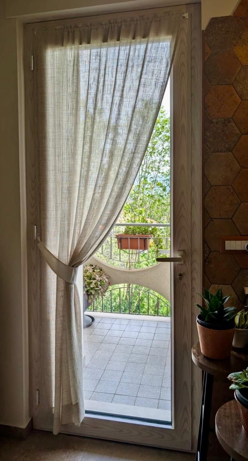 Porte a vetri aperte conducono a un patio piastrellato e a una siepe verde all'esterno, inondati dalla luce del sole.