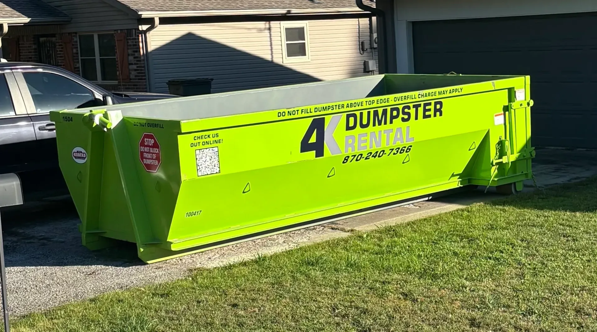 A green dumpster is parked in front of a house.