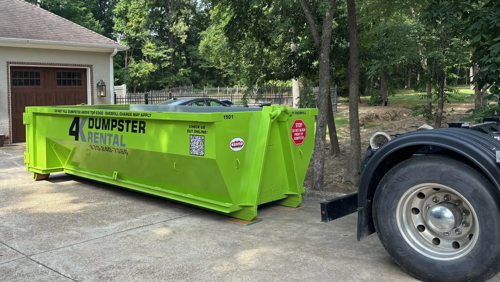 A green dumpster is parked in front of a house.
