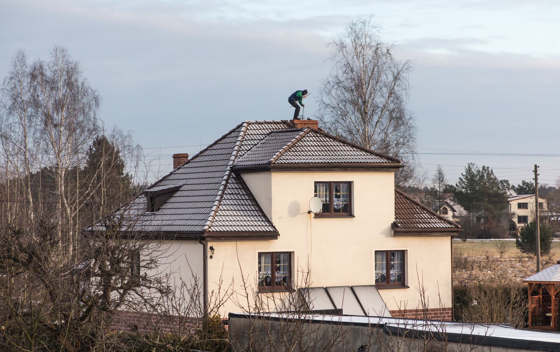 Technician standing on a rooftop cleaning and inspecting a brick chimney.