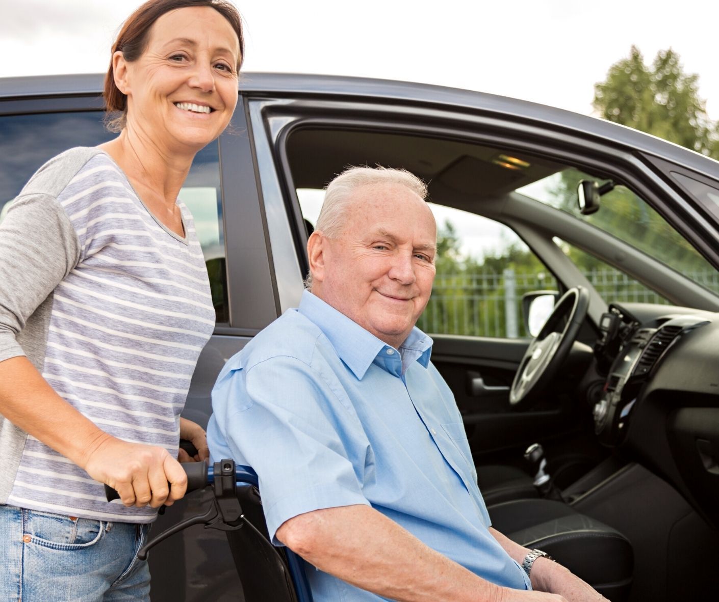 Smiling couple beside an open car door, with the man seated in the driver's seat