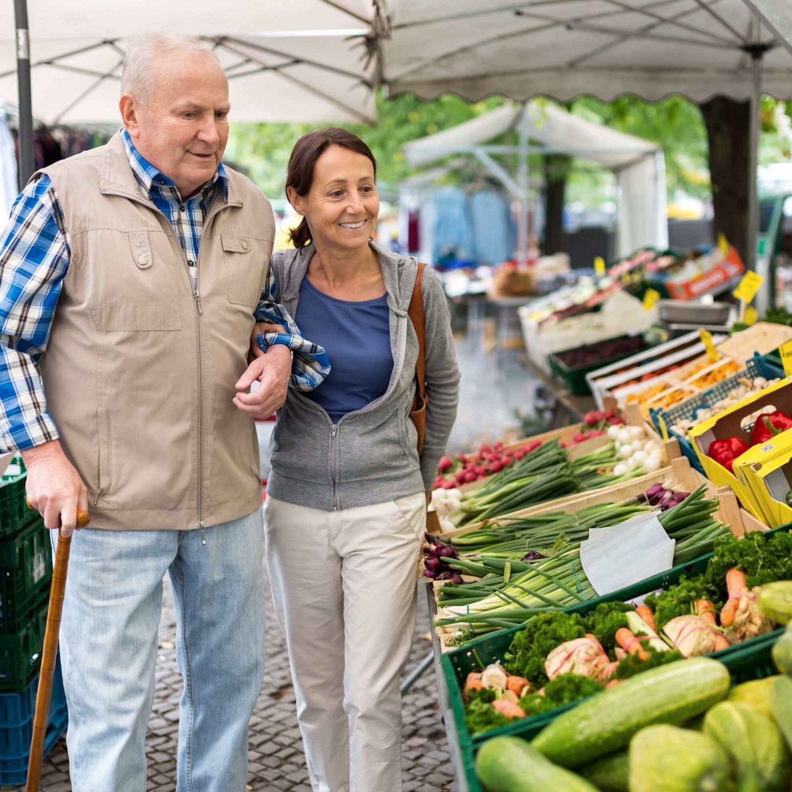 Two people browsing fresh vegetables at an outdoor market stall