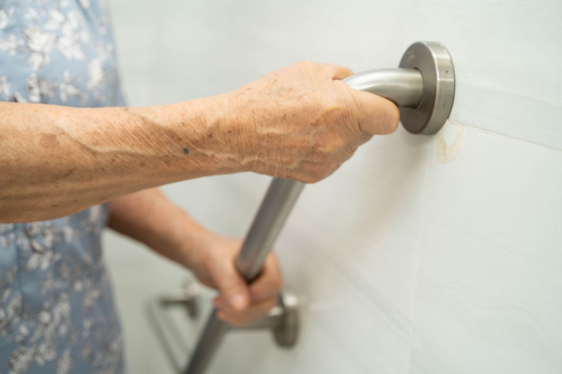 Hand gripping a stainless steel grab bar in a shower or bathroom area