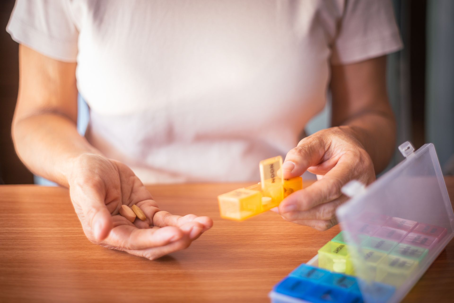Hands sorting colorful pills into a weekly pill organizer on a wooden table