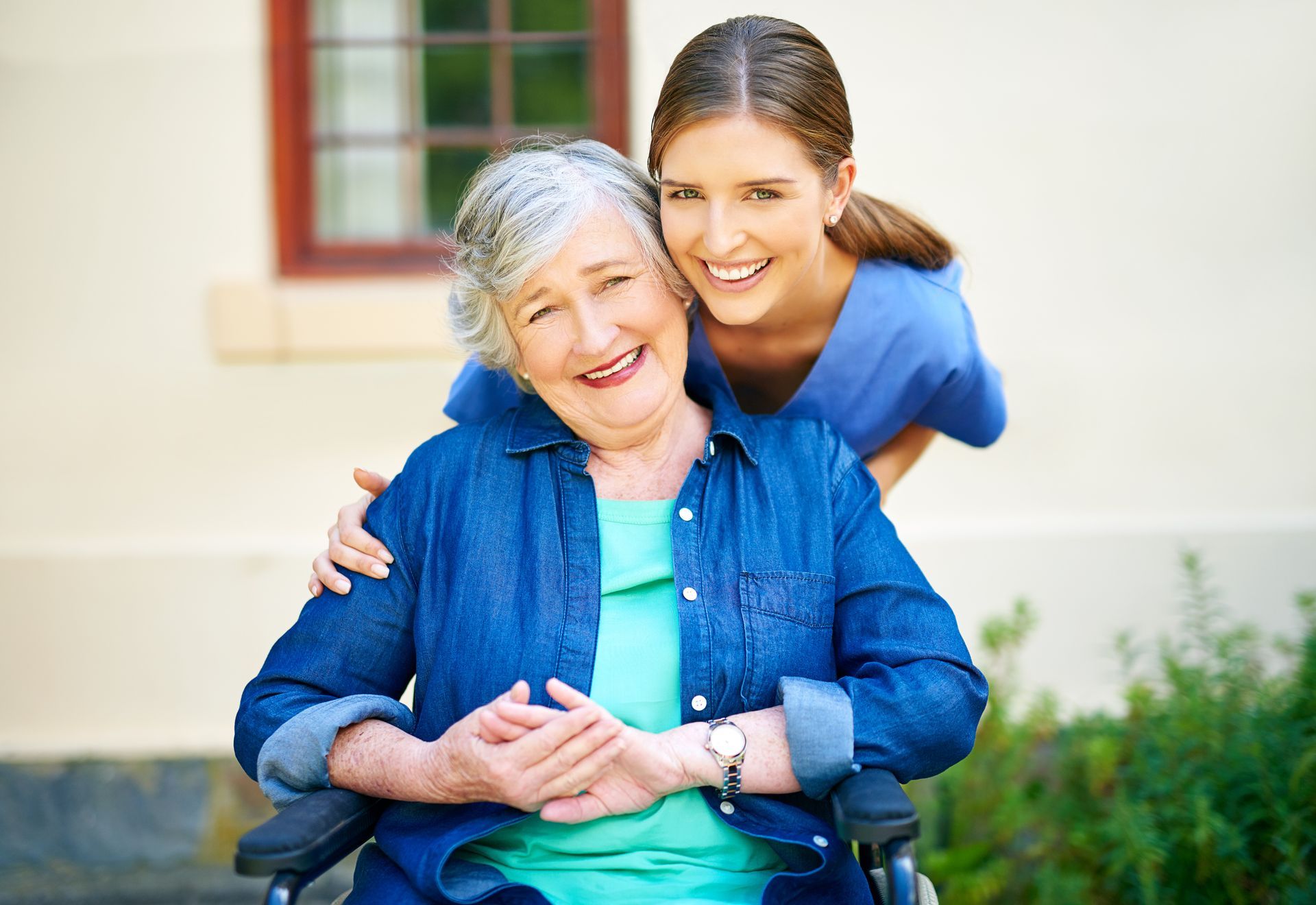 A young woman is standing next to an older woman in a wheelchair.
