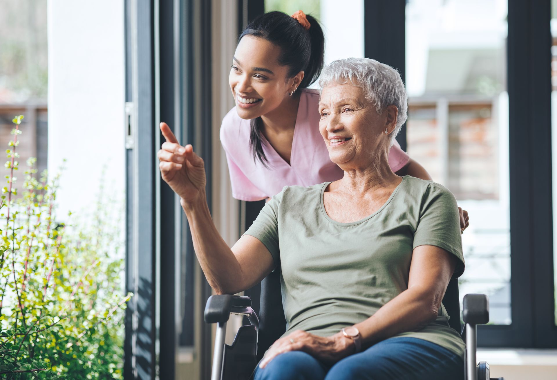 An elderly woman in a wheelchair is being helped by a nurse.