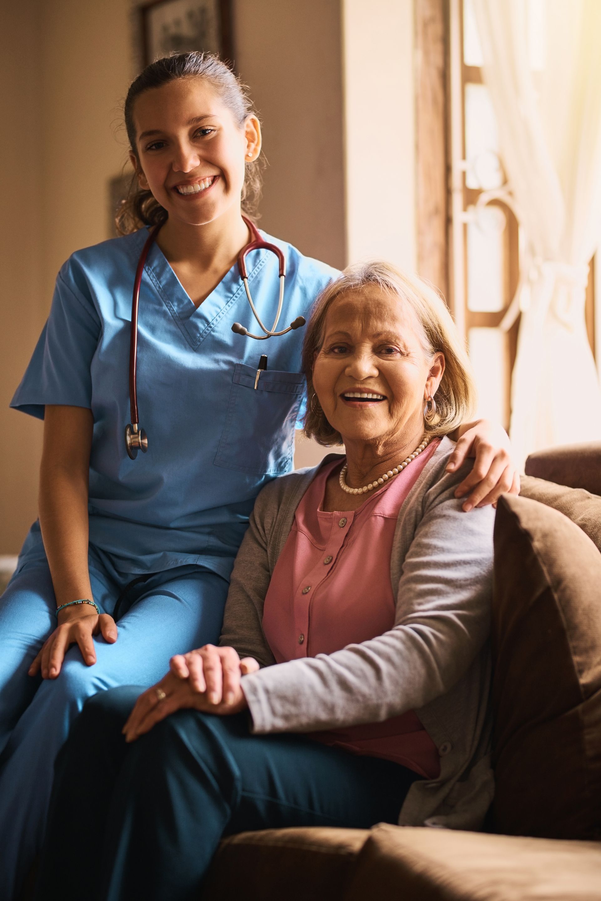 A nurse is sitting on a couch next to an elderly woman.