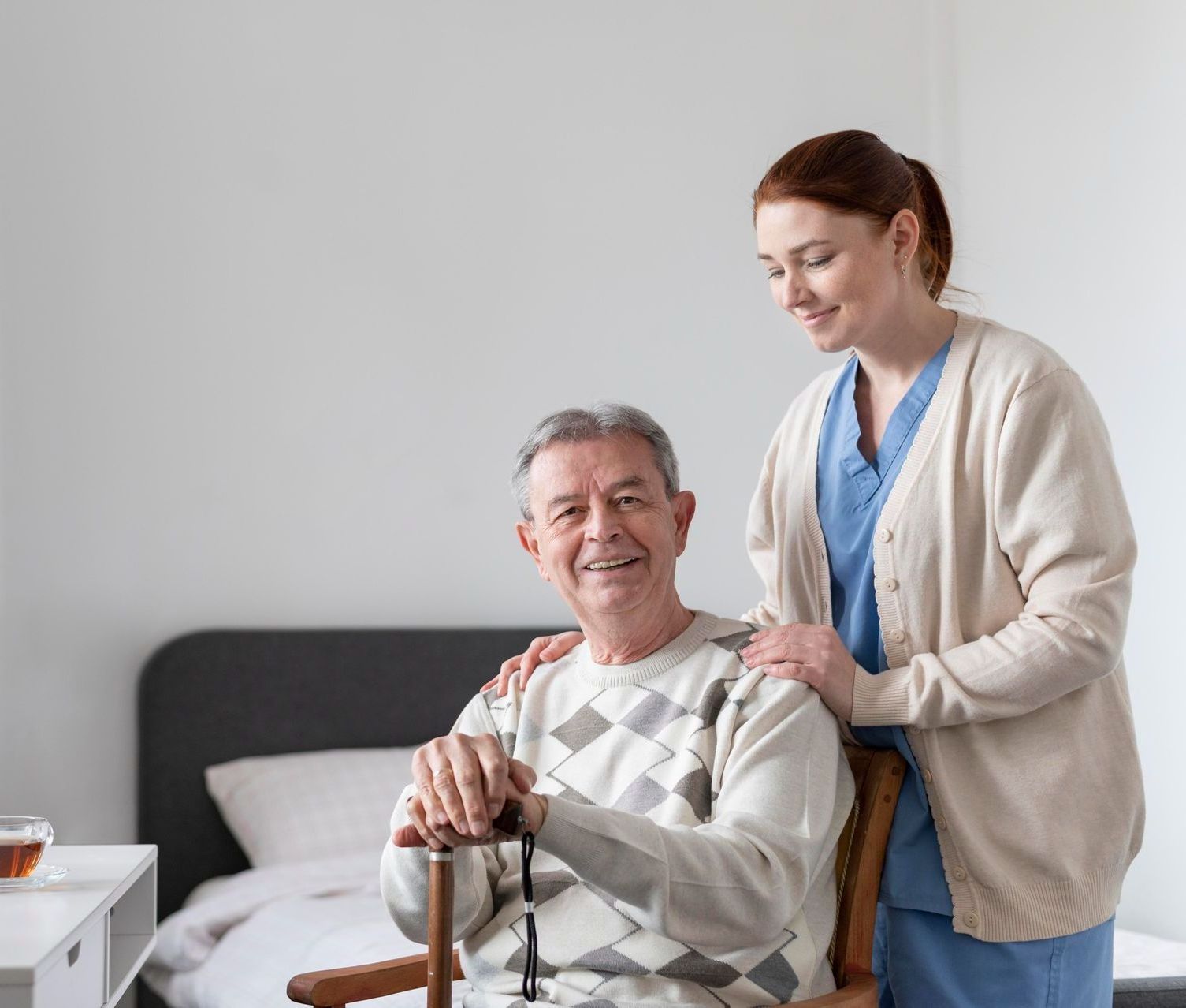 A woman is standing next to an elderly man in a wheelchair.