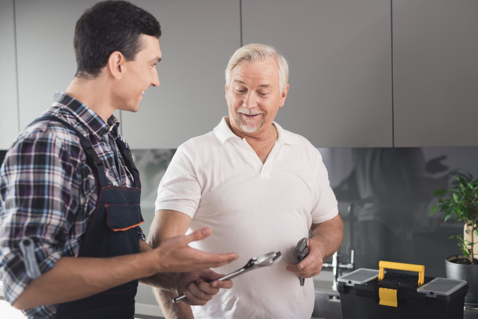 A plumber is talking to an older man in a kitchen.