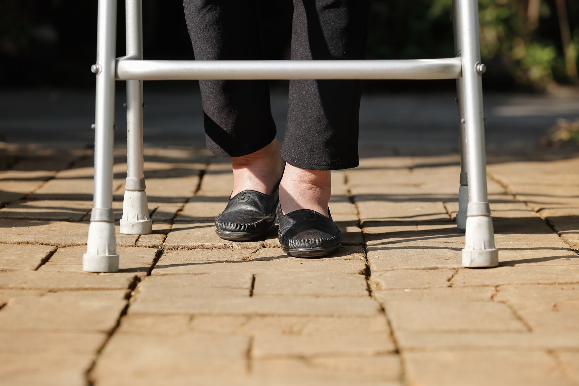Person using a walker on a paved path, wearing black shoes and dark pants.