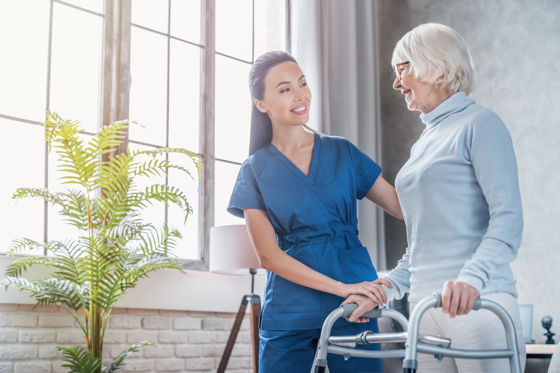 Caregiver assisting an older woman using a walker in a sunlit room.