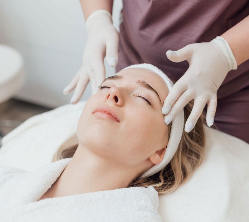 A person receives a facial treatment while lying on a spa bed, with hands in white gloves massaging their forehead.