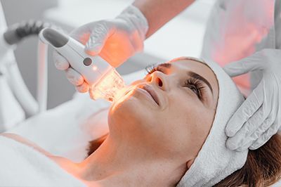 Facial treatment with a glowing handheld device on a woman’s face in a spa setting