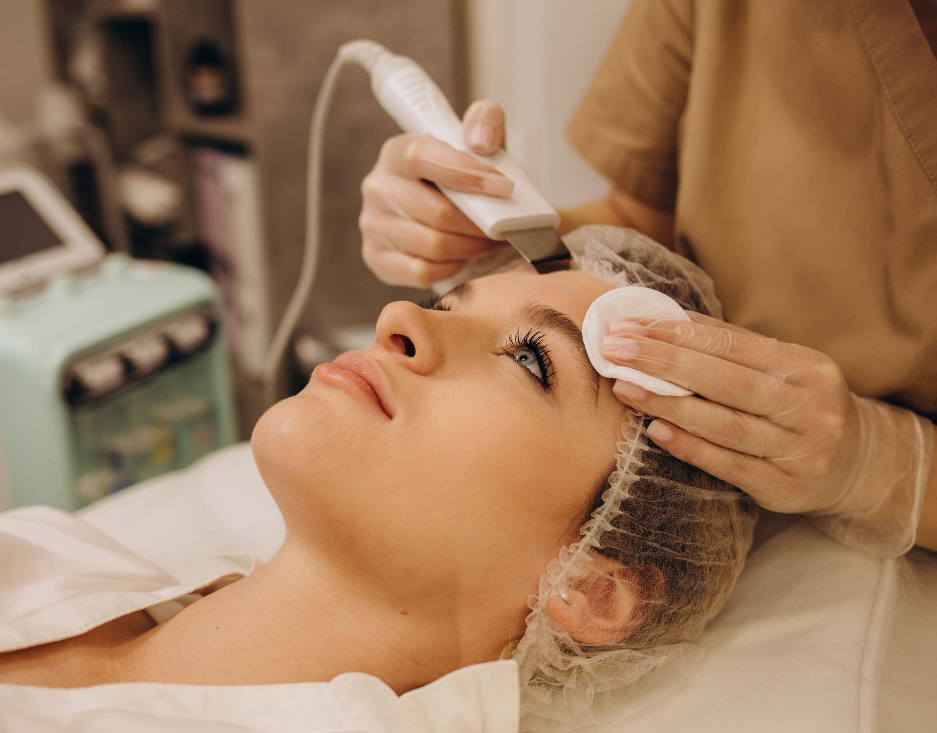 An esthetician uses an ultrasonic skin spatula on a client's forehead during a professional facial treatment.