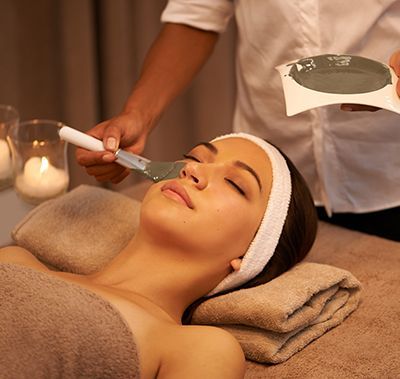 Facial spa treatment with cream being applied to a relaxed client in a warm, candlelit room