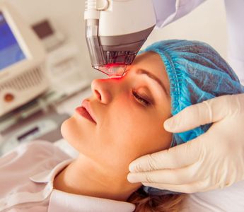 A technician uses a laser device on a patient's forehead during a cosmetic dermatology procedure.