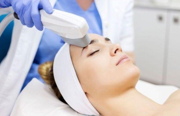 Cosmetic treatment with a handheld device applied to a woman’s forehead in a spa setting