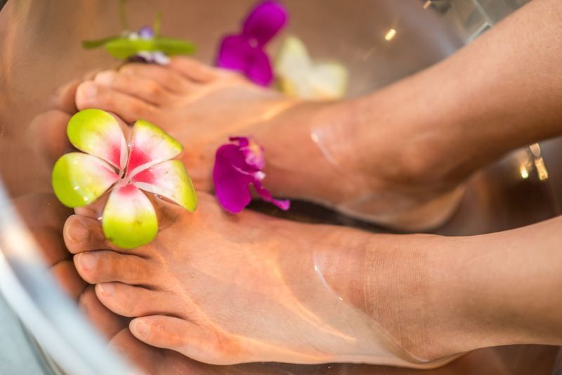 Feet soaking in a bowl of water decorated with colorful tropical flowers.